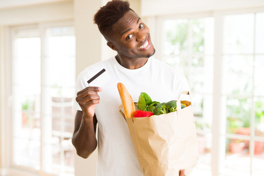 African american man holding paper bag full of groceries and holding credit card as payment