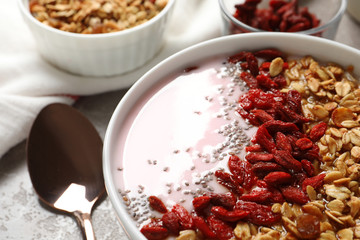 Smoothie bowl with goji berries and spoon on beige marble table, closeup