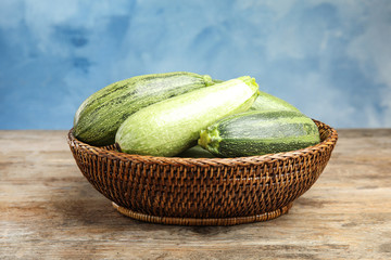 Wicker bowl with fresh ripe green zucchini on wooden table against blue background