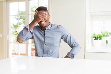 Fototapeta premium Handsome african american man on white table smiling and laughing with hand on face covering eyes for surprise. Blind concept.