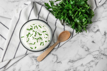 Fototapeta na wymiar Glass bowl of fresh sour cream with parsley and wooden spoon on marble table, flat lay. Space for text