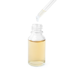Dripping essential oil from pipette into glass bottle on white background