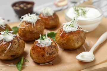 Fototapeta na wymiar Delicious baked potato with sour cream on wooden board, closeup