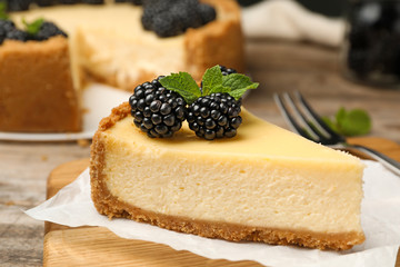 Piece of delicious cheesecake decorated with blackberries on table