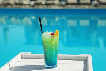 Refreshing cocktail on wooden table near swimming pool outdoors
