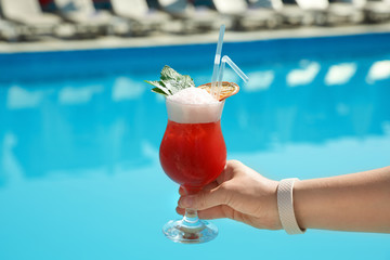 Woman with refreshing cocktail near swimming pool outdoors, closeup