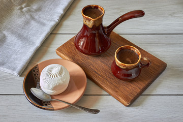 cup of coffee with cezve and marshmallow on a wooden table