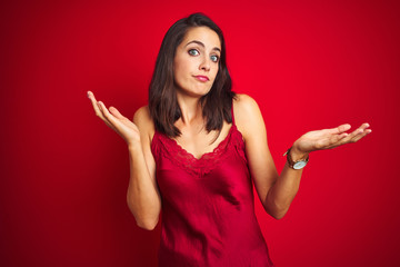 Young beautiful woman wearing sexy lingerie over red isolated background clueless and confused...