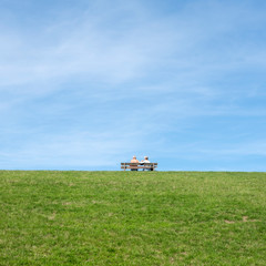 Fototapeta premium couple sit together on bench placed on top of grassy dike in friesland