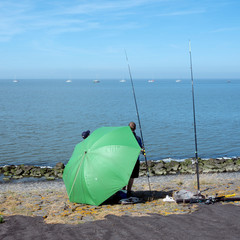 men behind large green umbrella seek protection from the sun white fishing in waddenzee near harlingen in the netherlands