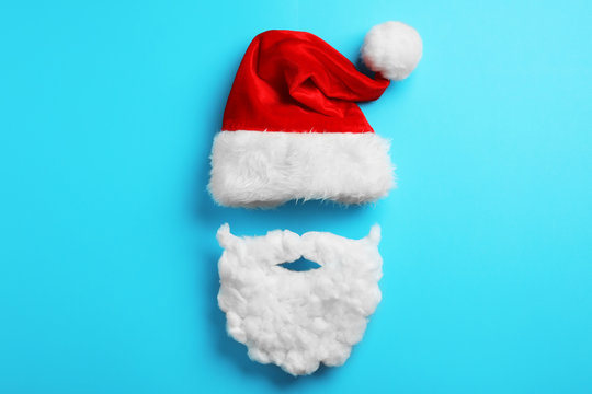 Santa Claus hat and beard on light blue background, flat lay