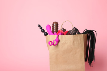 Paper shopping bag with different sex toys on pink background. Space for text