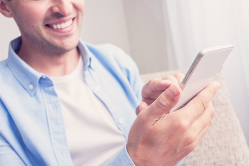 Young attractive man uses a smartphone. Men's hands, close up, cropped image, toned