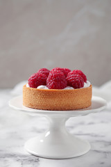 Cake stand with raspberry tart on marble table against light background. Delicious pastries