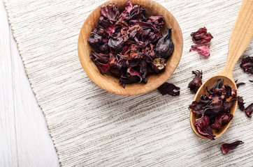 Top view at wooden bowl and spoon of dry hibiscus petals on linen cloth background