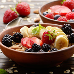Fruit healthy muesli with banana strawberry almonds and blackberry in clay dish on wooden kitchen table