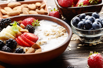 Fruit healthy muesli with banana strawberry almonds and blackberry with yogurt  in clay dish on wooden kitchen table