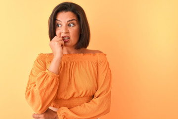 Young beautiful woman wearing casual t-shirt standing over isolated orange background looking stressed and nervous with hands on mouth biting nails. Anxiety problem.