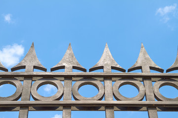 Schwarze Spitzen eines massiven Eisenzaunes ragen in den Himmel.