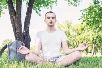 Naklejka na ściany i meble Handsome young guy sitting in Park in summer, man meditates with his eyes closed, portrait, toned