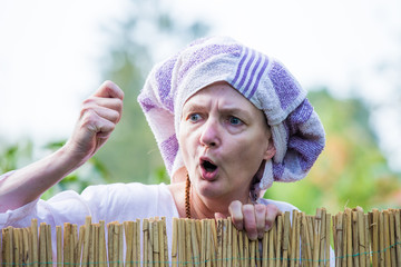 An angry woman in a headscarf looks over a garden fence and scolds. Concept problematic...