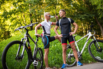 Obraz premium Athletic man and woman with bicycles posing in the park on a background of green knoll.