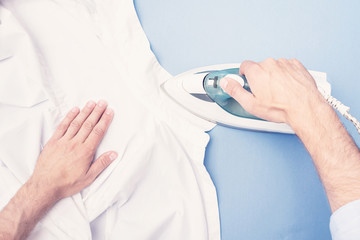 Man ironing clean shirt, men's hands, closeup, top view, toned