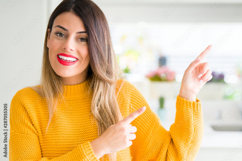 Canvas Prints Young beautiful woman wearing winter sweater at home smiling and looking at the camera pointing with two hands and fingers to the side.