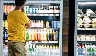 man alone and isolated at the supermarket or minimarket choosing his drink or snack in big fridge...