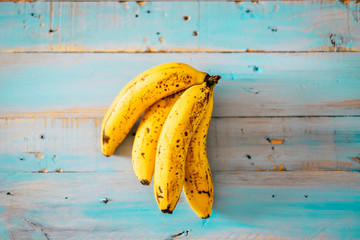 closeup of yellow and marron bananas on a blue table of wood - diet and healthy and vegetarian or vegan lifestyle - potassium and seasonal food concept in vertical view