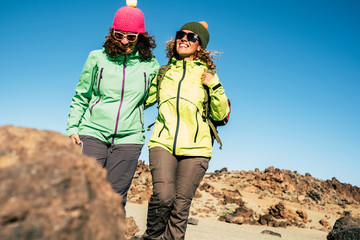 two friends walking and hiking together at the mountain with the rocks and the cold - wearing green sweater for the  winter season - trip and adventure in outdoor leisure  activity