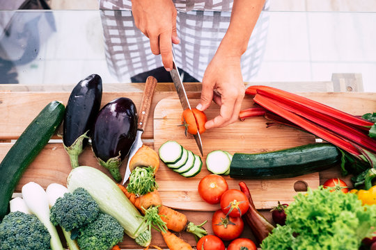 closeup of table full of vegetables like tomatoes, carrots and more - adult or senior cutting food inthe kitchen at home or restaurant - vegan and vegetarian lifestyle and diet