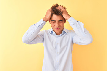 Young handsome businessman wearing elegant shirt over isolated yellow background suffering from headache desperate and stressed because pain and migraine. Hands on head.