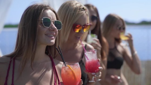 Medium close-up shot of four sexy beautiful models in bikinis sipping from a tropical cocktail drink