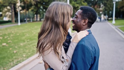 Charming mixed race couple in public park. Caucasian female whispering to ear of her black male and they kiss - Powered by Adobe