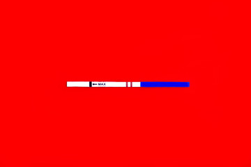 A strip test for pregnancy with a positive result against a red background.