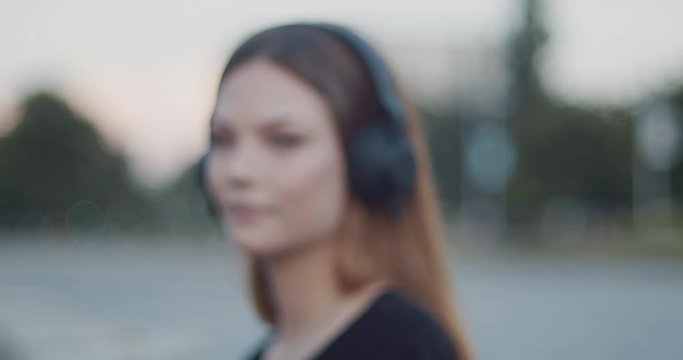Young woman listening to music on black headphones - defocused blurry effect slow motion