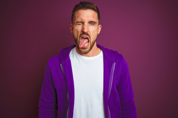 Young fitness man wearing casual sports sweatshirt over purple isolated background sticking tongue out happy with funny expression. Emotion concept.