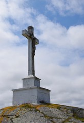 side view of a large crucifix on top of a hill, clouds in the background  