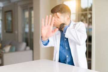 Fototapeta premium Young handsome doctor man at the clinic covering eyes with hands and doing stop gesture with sad and fear expression. Embarrassed and negative concept.