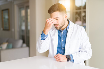 Young handsome doctor man at the clinic tired rubbing nose and eyes feeling fatigue and headache. Stress and frustration concept.