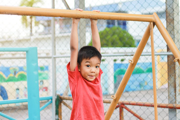 Obraz premium Kid exercise for health and sport concept. Happy Asian child boy playing and hanging from a steel bar at the playground. 5 years old.