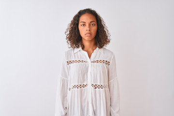 Young brazilian woman wearing shirt standing over isolated white background with serious expression on face. Simple and natural looking at the camera.