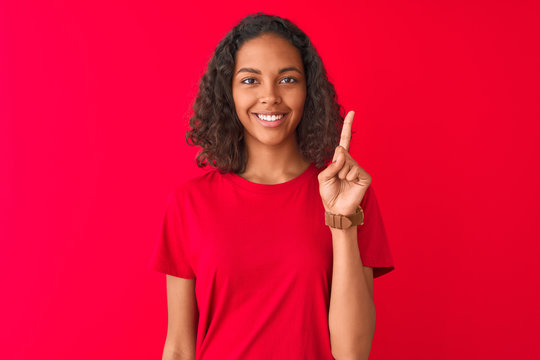 Young brazilian woman wearing t-shirt standing over isolated red background surprised with an idea or question pointing finger with happy face, number one