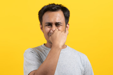 Face expression of human.  Asian male smelling disgusted odor and pinching his nose in studio shoot yellow background.