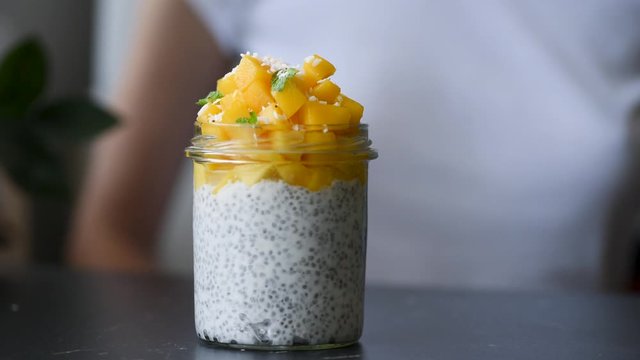 Chia pudding with mango cubes in jar. Woman hands push forward glass with chia pudding. Healthy food, healthy lifestyle, clean eating concept