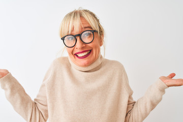 Middle age woman wearing turtleneck sweater and glasses over isolated white background clueless and confused expression with arms and hands raised. Doubt concept.