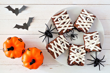 Halloween mummy brownies, above view with decor on a white wood background