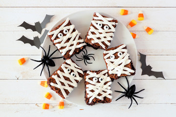 Plate of Halloween mummy brownies, top view with decor on a white wood background