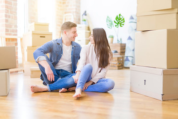 Young beautiful couple relaxing sitting on the floor around cardboard boxes at home, smiling happy moving to a new house